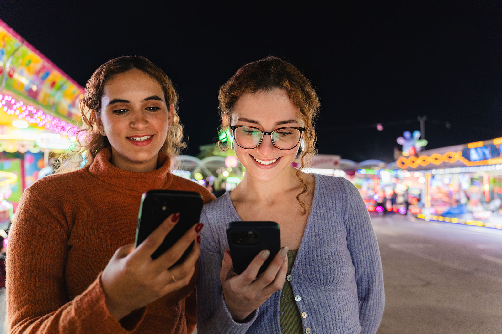 Two women playing Promo on Demand games on their cell phones at a fairground