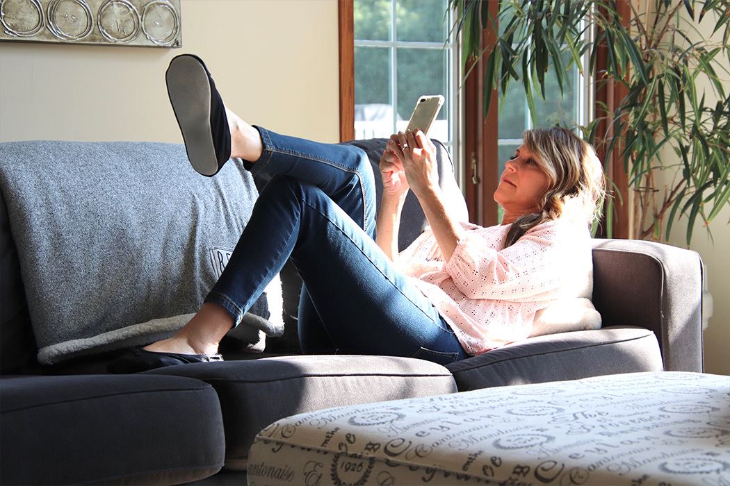 A woman relaxing on her couch, playing games on her phone