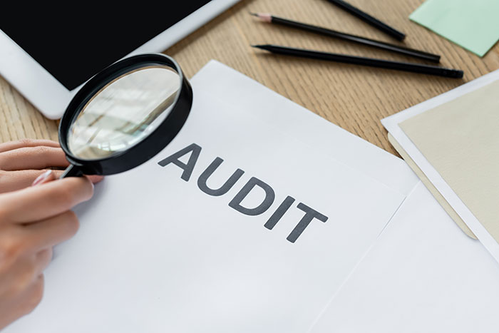 A person holding a magnifying glass over an audit document